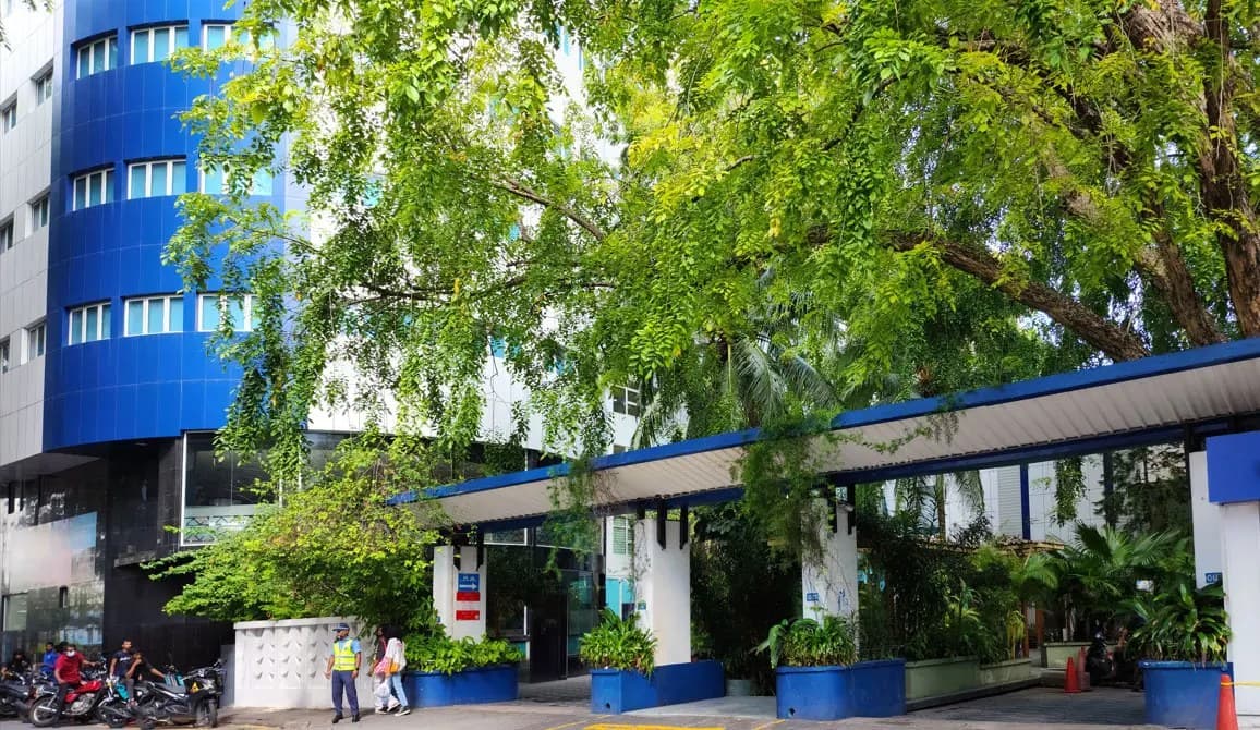 The entrance of ADK Hospital: its blue tower and covered walkway behind a canopy of trees